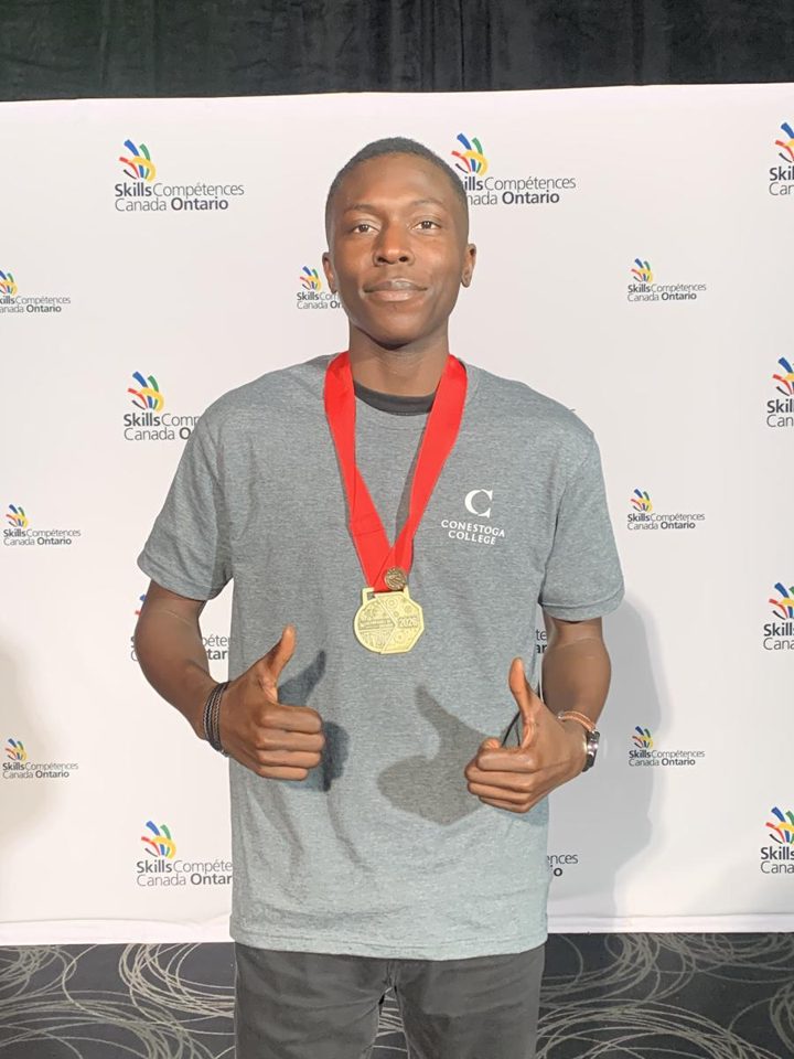 Ayo Osota wearing a gold medal in front of a Skills Canada Ontario banner